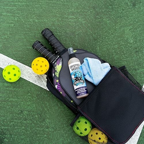 Pickleball equipment with paddles, balls, spray, and towel on court.